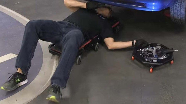 Mechanic using Eastwood rolling undercar tool tray to access tools while working under a car