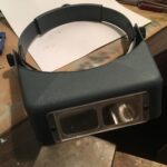 OptiVisor head-mounted magnifier with glass lenses providing clear and magnified vision for detailed toy car restoration work.