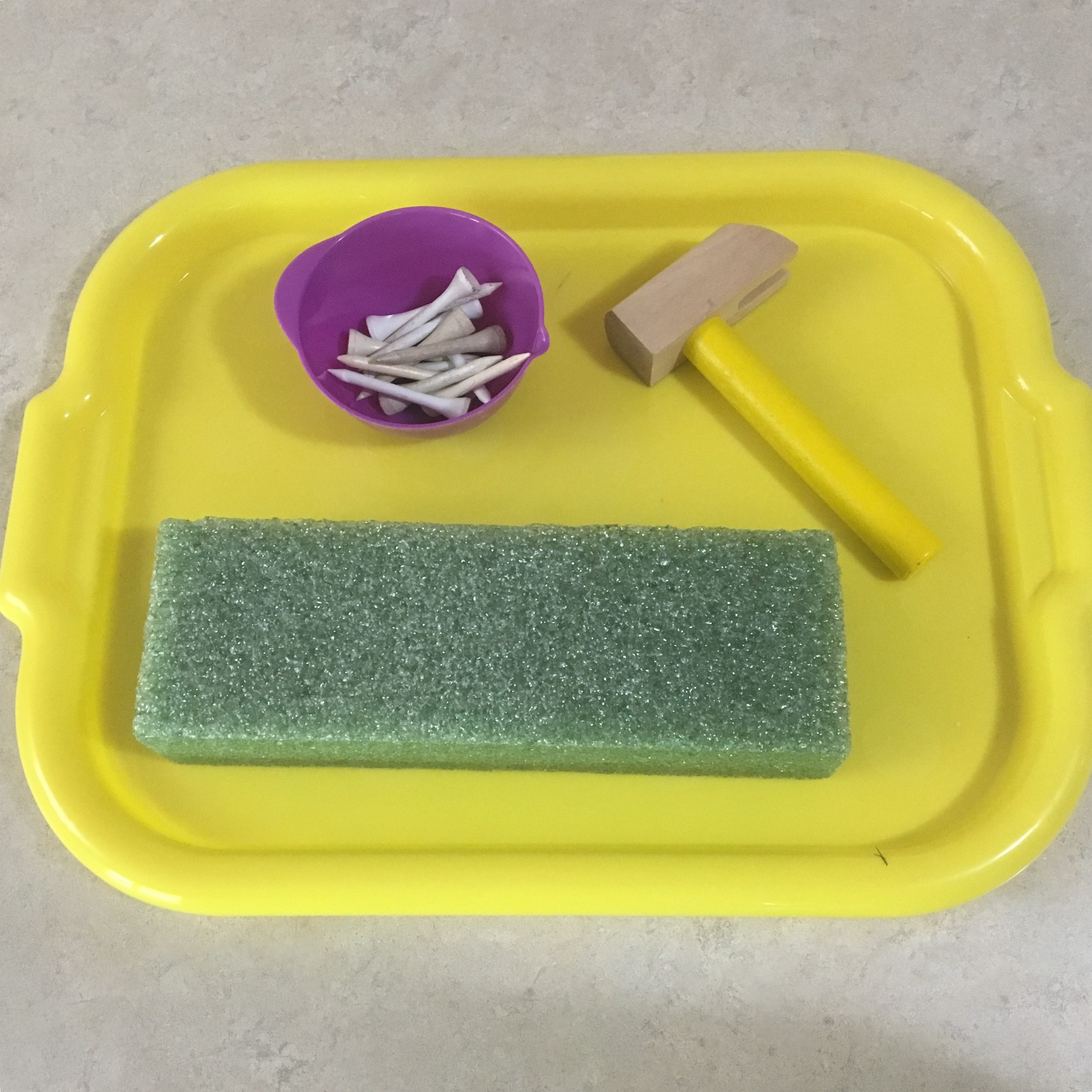 Toddler engrossed in hammering golf tees into a foam block, a fun activity using a play tool kit hammer.